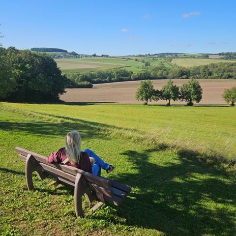 Eine Frau sitzt auf einer Bank und genießt den Weitblick in die grüne Natur