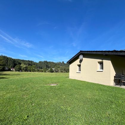 Ein gemütliches Haus in einer grünen Landschaft. Der Himmel ist blau und die Umgebung wirkt einladend und ruhig.