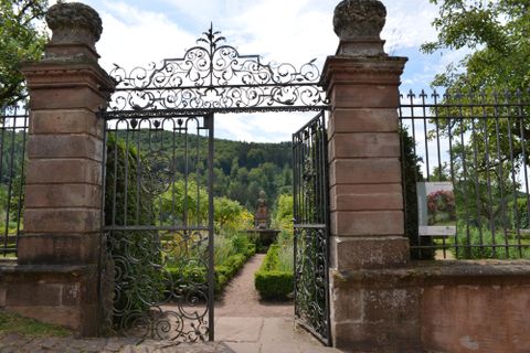 A beautiful garden with a wrought-iron gate and lush greenery. In the background, hills and trees are visible.