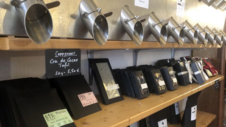 Ein Regal mit Schokoladentafeln und Kakaopulver in verschiedenen Behältern. Die Produkte sind in eleganten Verpackungen und preisschildern angeordnet.