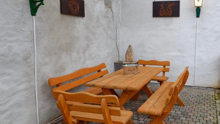 Ein Holztablett mit passenden Bänken steht in einem gepflasterten Innenhof. An den Wänden hängen dekorative Tafeln und laternenartige Leuchten.