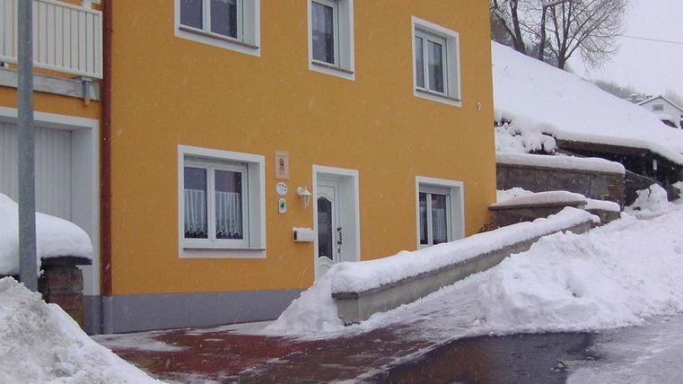 Ein gelbes Haus steht in einer schneebedeckten Landschaft. Der Schnee liegt auf dem Boden und die Umgebung ist winterlich.