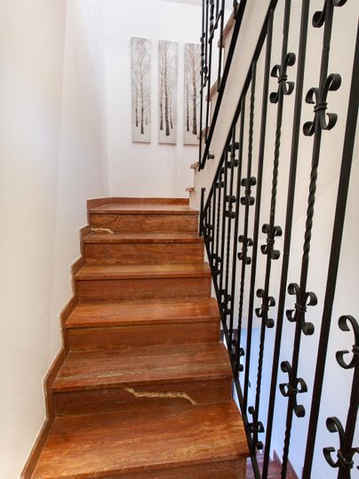 Eine Holztreppe mit einem schmiedeeisernen Geländer führt nach oben. An der Wand hängen drei Bilder von Bäumen.