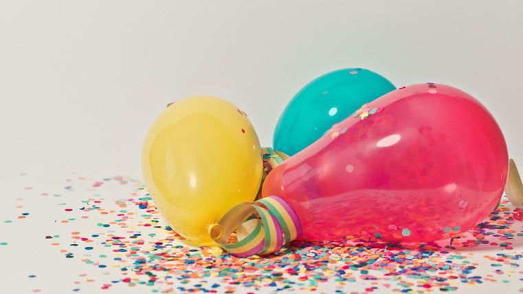 Bunte Ballons liegen auf einem Konfetti-Haufen. Sie schaffen eine festliche und fröhliche Atmosphäre.