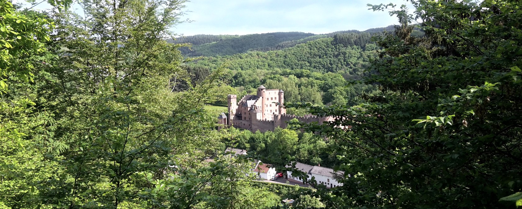 Schloss Hamm thront malerisch inmitten grüner Wälder und Hügel, umgeben von üppiger Vegetation und einem klaren Himmel., © TI Bitburger Land