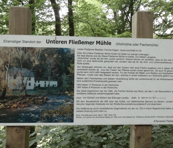 Ein Schild im Wald informiert über die Untere Fließemer Mühle. Es zeigt ein Bild der Mühle und enthält historische Details zur Nutzung und Geschichte., © TI Bitburger Land