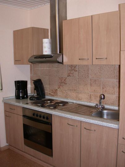 A modern kitchen with wooden cabinets, a sink, and a stove. The amenities also include a kettle and a coffee machine.