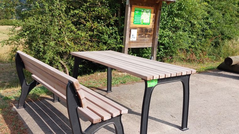 Picknicktisch und Bank neben einer Infotafel im Freien.