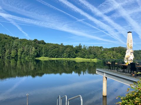 Stausee Bitburg mit Terrasse und Sonnenschirm am Ufer.