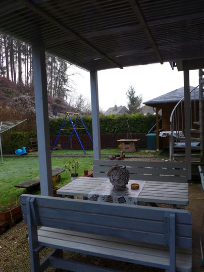 A cozy garden with a wooden table and benches. In the background, a playground and a pavilion are visible.