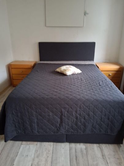 Ein schlichtes Schlafzimmer mit einem großen Bett und zwei Holz-Nachttischen. Auf dem Bett liegt ein Kissen in der Mitte.