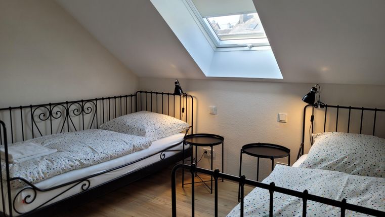 Ein gemütliches Schlafzimmer mit zwei Einzelbetten und Fensterlicht. Die Wände sind schlicht und die Möbel sind aus schwarzem Metall.