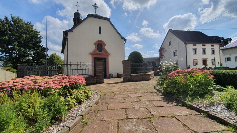 L'église du village de Sefferweich avec ses parterres de fleurs et son chemin pavé.