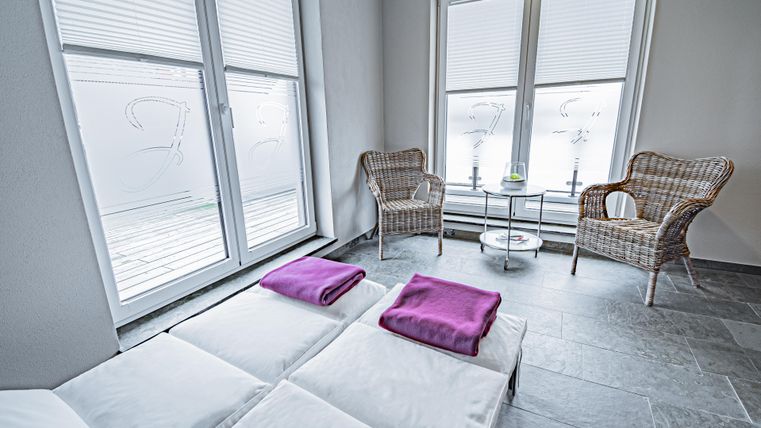 A quiet room with two loungers and purple towels. Two wicker chairs and a small table are next to large windows.