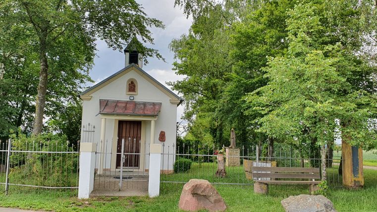 Kleine Kapelle mit Zaun und Bäumen im Hintergrund.