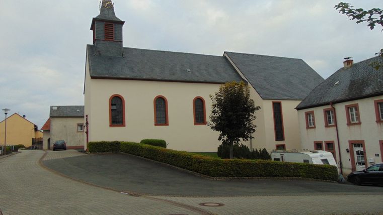 Kirche St. Urban mit Turm und umliegenden Gebäuden auf einem Dorfplatz.