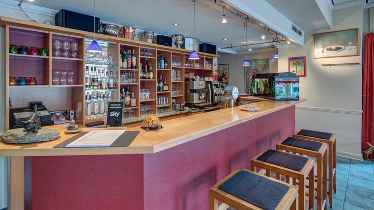 Eine moderne Bar mit Holzregalen und einer Theke. Im Hintergrund sind verschiedene Getränke und eine kleine Aquarienlandschaft sichtbar.