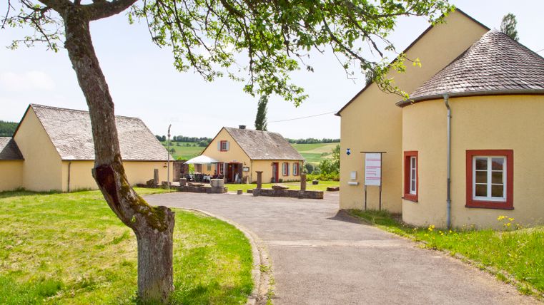 Römische Villa Ortrang in Fließem mit gelben Gebäuden und grünem Baum im Vordergrund.