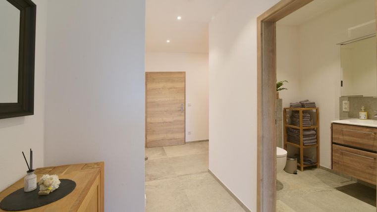 Ein heller und moderner Flur mit einem Holzschrank und einem Spiegel. Rechts sieht man einen Zugang zu einem Badezimmer.