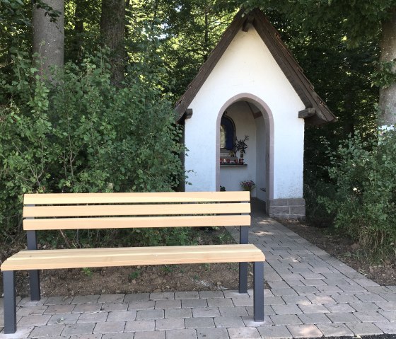 Une petite chapelle blanche au toit marron se dresse &agrave; la lisi&egrave;re de la for&ecirc;t. Devant, un banc en bois sur un chemin pav&eacute;., &copy; TI Bitburger Land