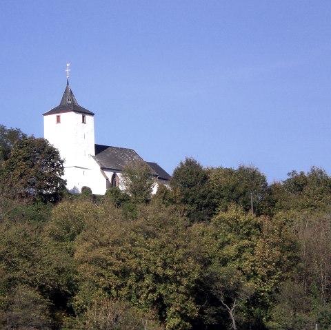 Die Kirche St. Apollonia in Gransdorf thront auf einem bewaldeten Hügel unter klarem, blauem Himmel., © Doris Pauels