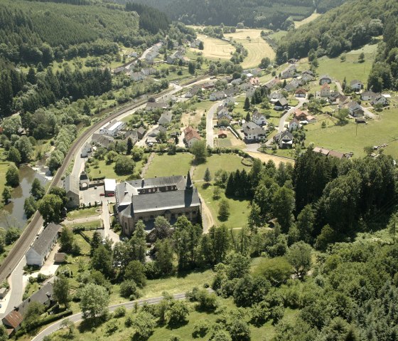 Aerial view of a village with a church in the foreground, surrounded by woods and fields. A railroad line runs through the village., © Rudolf Höser