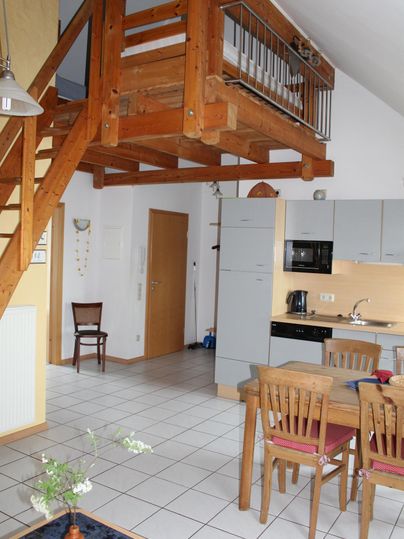Eine helle Wohnung mit offenem Grundriss, die eine Holztreppe und einen Essbereich zeigt. Die Küche ist modern und gut ausgestattet.