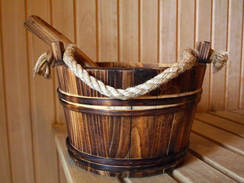 A wooden container with a rope handle stands on a bench in the sauna. The container is traditional and is used for storing water or essences.