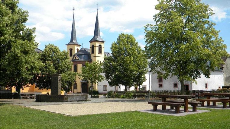 Dorpsplein met kerk en bomen in Idenheim.