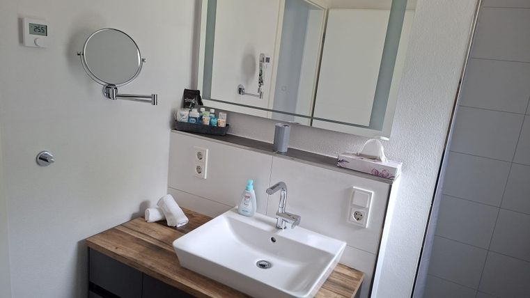 Une salle de bain moderne avec un lavabo sur une étagère en bois. En arrière-plan, des serviettes et divers produits de soin sont visibles.