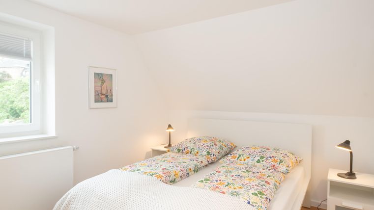 Een heldere slaapkamer met een tweepersoonsbed en kleurrijke dekbedden. Aan de muur hangt een schilderij, en er zijn twee nachtlampen.
