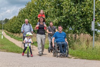 Eine Familie, teilweise mit Rollstuhl und Laufrad, ist in der Natur unterwegs