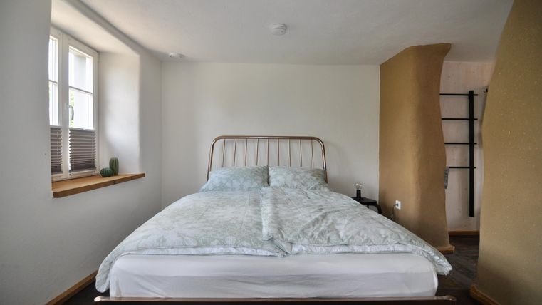 A simple bedroom with a bed and light walls. The room has a window and a cozy atmosphere.