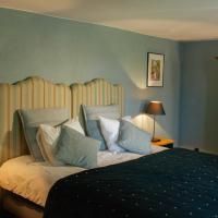 Une chambre confortable avec un grand lit et des coussins élégants. Les murs sont peints dans des teintes douces de bleu et pastel, et une table de chevet avec une lampe se trouve à côté du lit.