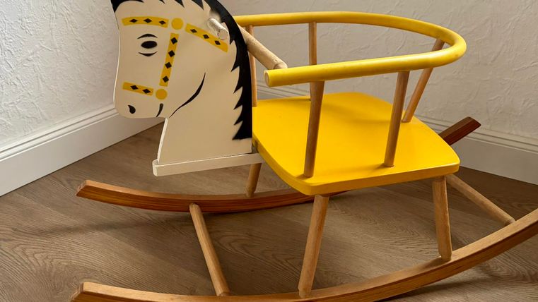 Un cheval à bascule créatif en bois avec une selle jaune et une tête au design amical. Il se trouve sur un parquet en bois dans une pièce lumineuse.