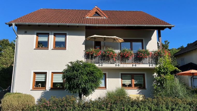 Een mooi huis met een rood dak en aangrenzende bloembakken. De tuin is groen en goed onderhouden, met struiken en een kleine boom.