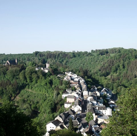 Panoramisch uitzicht op Kyllburg met kerk en huizen, ingebed in groene bossen en heuvels onder een heldere hemel., © TI Bitburger Land