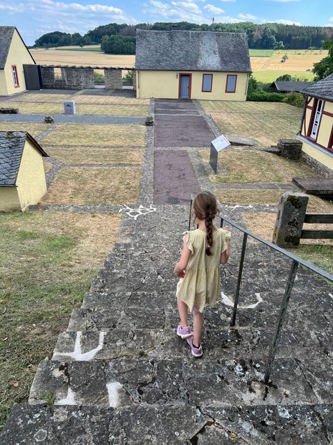 ein Kind geht eine Steintreppe runter auf dem Geländer der Römisches Villa Otrang in Fließem. Dort stehen Schutzhäuser, in denen Mosaike sind