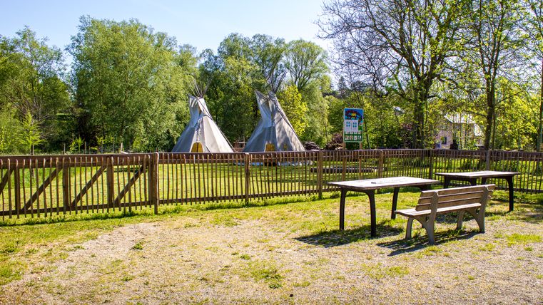 Spielplatz mit Tipis und Holzzaun, umgeben von Bäumen.