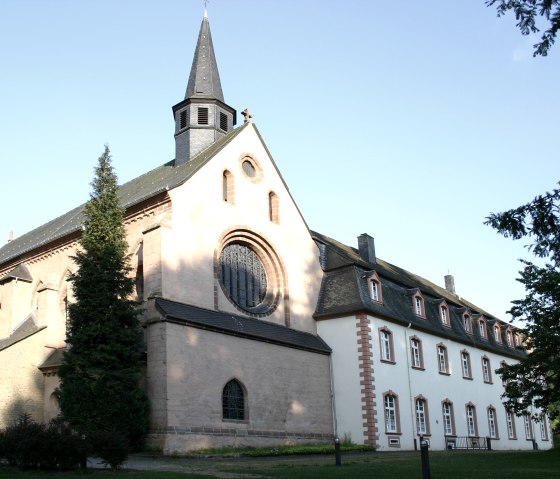 Das St. Thomas Kloster zeigt gotische Architektur mit einem Rosettenfenster und einem kleinen Turm. Es ist von Bäumen umgeben., © TI Bitburger Land