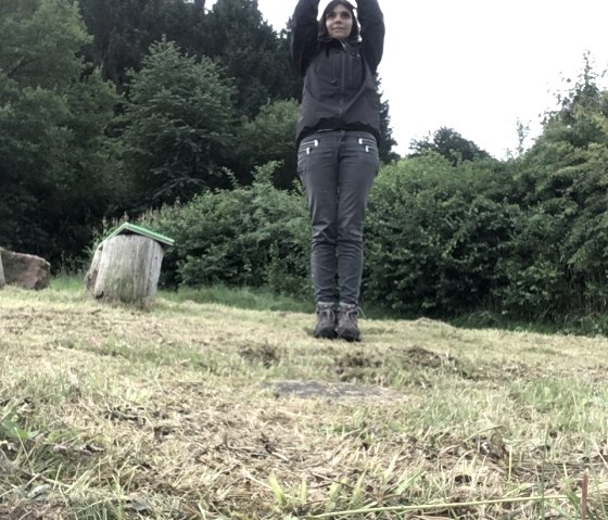 Person steht auf einer Wiese mit erhobenen Armen, umgeben von grünen Bäumen und Sträuchern., © TI Bitburger Land M.Mayer