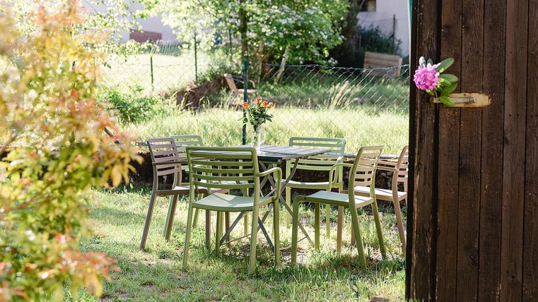 Ein einladender Garten mit einem Tisch und Stühlen aus Holz. Im Hintergrund sind Bäume und eine grüne Wiese sichtbar.