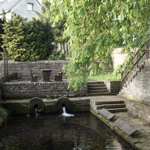 Alter Waschplatz mit Wasserbecken, Steinmauern und Treppen, umgeben von grüner Vegetation und Bäumen., © Monika Bach