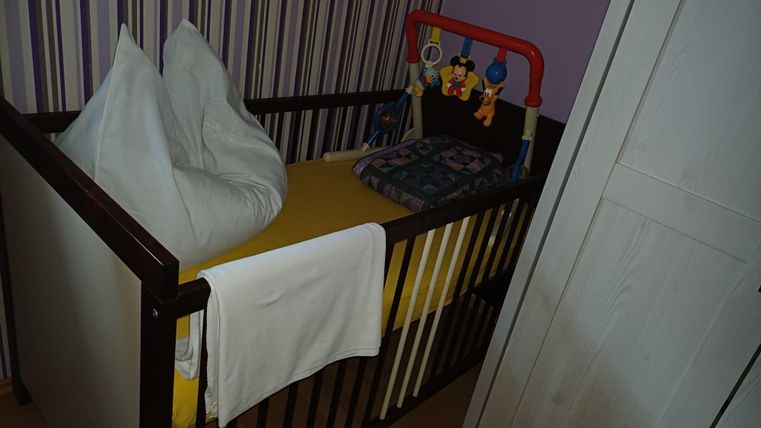 A child's bed with a yellow mattress and pillow. Colorful toys are hanging on the side.