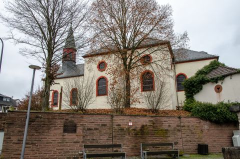 Church in Wißmannsdorf with trees and stone wall in the foreground.