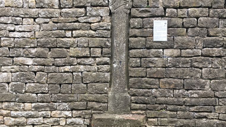 Steinmauer mit Kreuzwegstation und Infotafel.