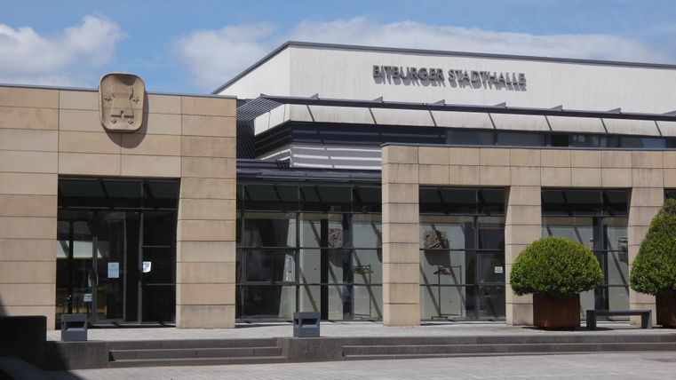 Une administration municipale moderne avec une façade claire et de grandes fenêtres. Devant le bâtiment, il y a des plantes bien entretenues.