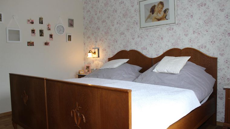 Une chambre confortable avec un grand lit en bois et des draps blancs. Des images et une horloge sont accrochées au mur, créant une atmosphère accueillante.