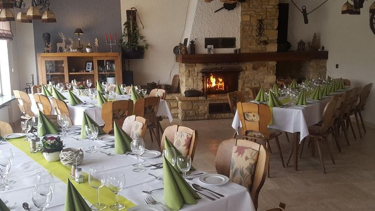 Ein gemütlicher Speisesaal mit eleganten Tischdecken und grünem Besteck. Im Hintergrund brennt ein Kamin, der eine einladende Atmosphäre schafft.