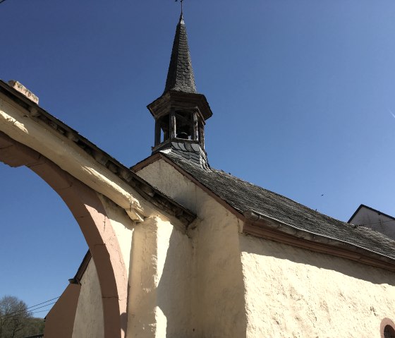 Eine kleine Kapelle in Birtlingen mit spitzem Turm und gelber Fassade vor klarem, blauem Himmel., © TI Bitburger Land